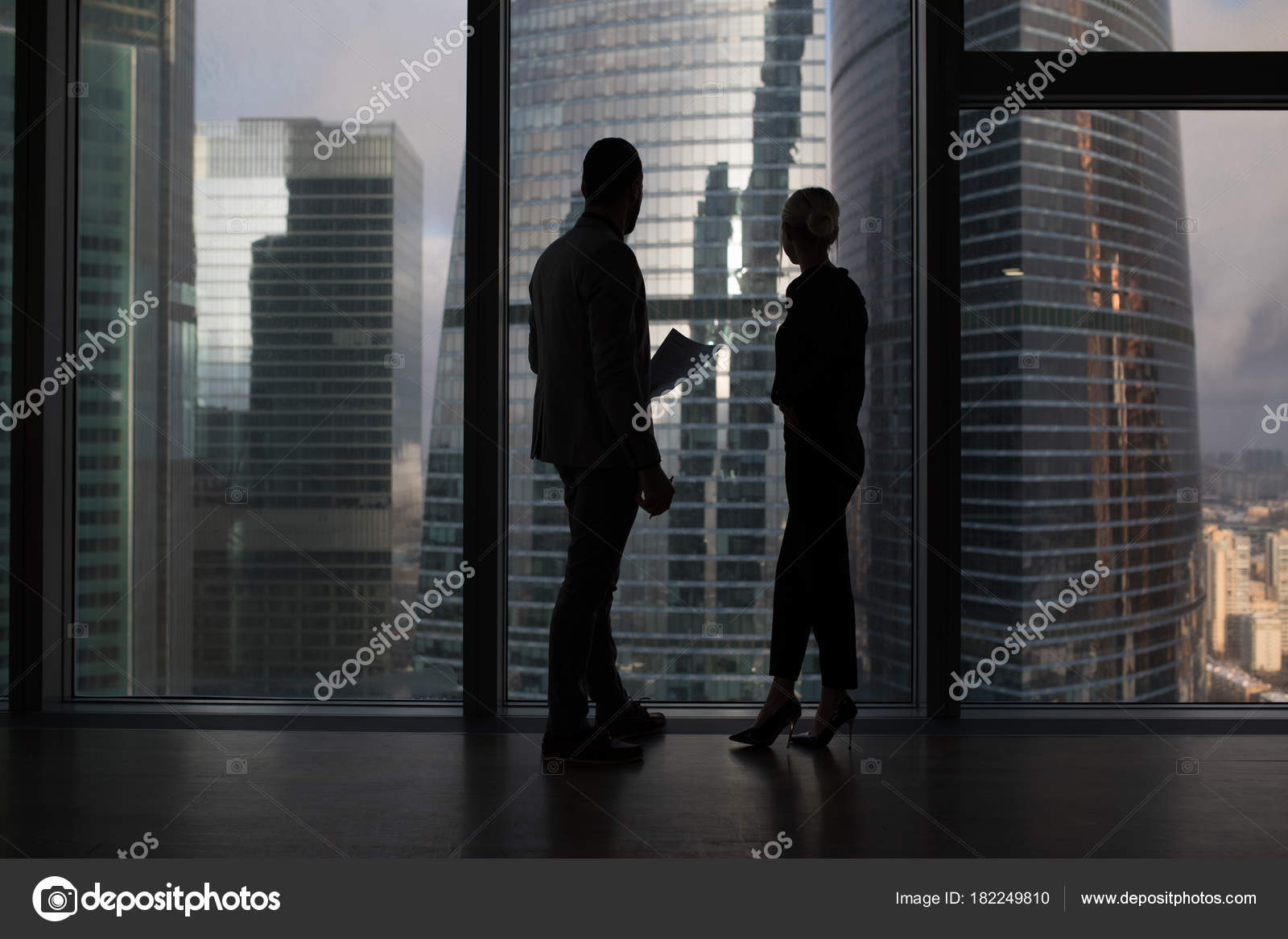Business people talking negotiating standing near large panoramic window with big city buildings. Business people talking negotiating standing near large panoramic window with big city buildings.