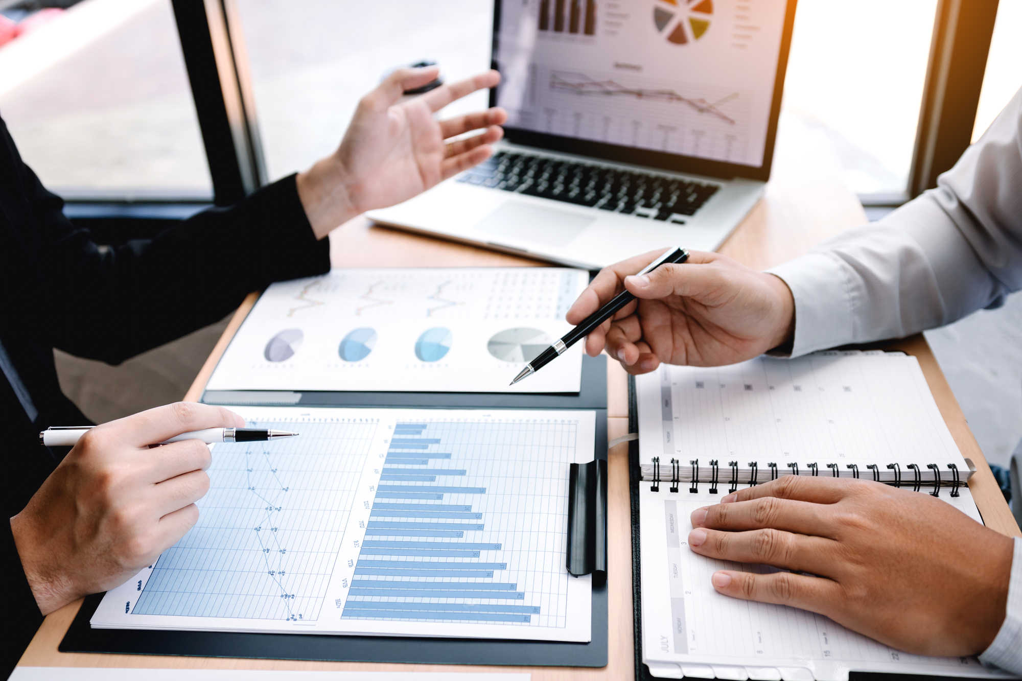 Male manager is explaining about the company's cost graph on the laptop computer for employees to listen to and share the analysis together.